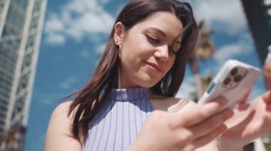 Neşeli esmer kadın dışarıda otururken telefonla mesaj atıyor.