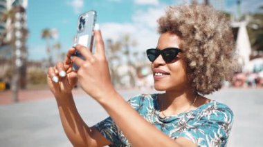 Neşeli Afrikalı gri saçlı kadın güneş gözlüğü takıyor, sokak sokak videolarını çekiyor.