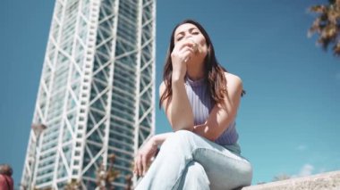 Dışarıda bankta otururken dondurma yiyen kumral kadın.
