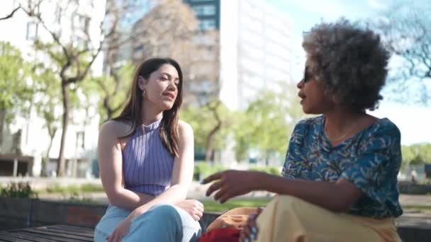 Dwie Pozytywne Wieloetniczne Kobiety Rozmawiające Podczas Siedzenia Ławce Zewnątrz — Wideo stockowe