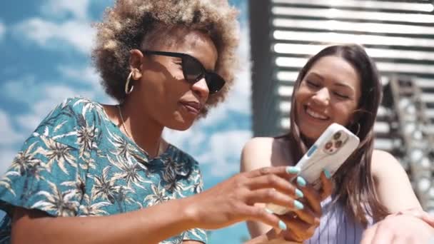 Rindo Mulheres Ensolaradas Falando Olhando Para Telefone Enquanto Sentado Livre — Vídeo de Stock