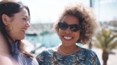 Çok ırklı iki yakışıklı kadın, yatların yakınındaki sette kamera önünde video çekiyor.