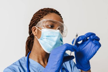 Beyaz arka planda izole edilmiş şırıngayla poz veren siyah maskeli bir doktor.