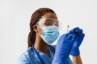 Beyaz arka planda izole edilmiş şırıngayla poz veren siyah maskeli bir doktor.