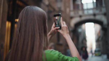 Yeşil tişört giyen güzel sarışın kadın dışarıda telefonla caddenin fotoğrafını çekiyor.