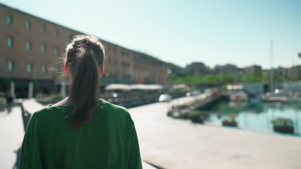 パンツブロンド女性身に着けている緑のTシャツ見ますビューでザ シーフロント近くヨット屋外 — ストック動画