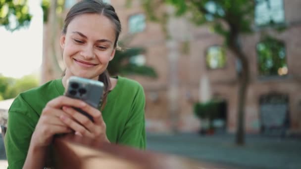 Smějící Blondýna Žena Zeleném Tričku Smskování Mobilu Lavičce Městě Venku — Stock video