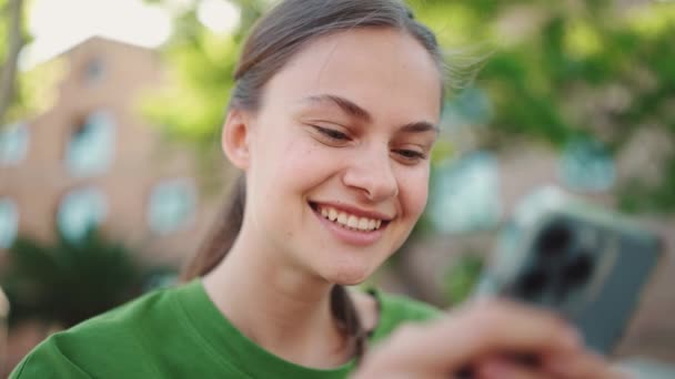 Smiling Blonde Woman Wearing Green Shirt Texting Phone Bench Outdoors — Stock Video