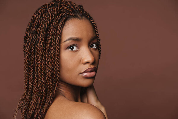 Half-naked black woman posing and looking at camera isolated over brown background