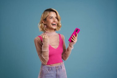 Mavi duvarda izole edilmiş cep telefonu kullanan genç bir kadın birinci sınıf jest yapıyor.