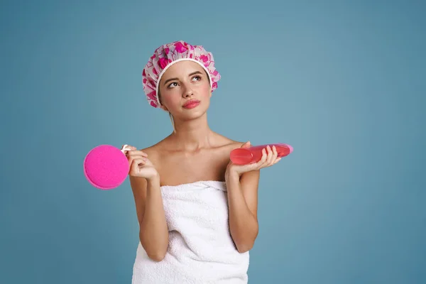 年轻女子裹着毛巾 摆出淋浴海绵和隔着蓝色墙壁的凝胶的姿势 — 图库照片