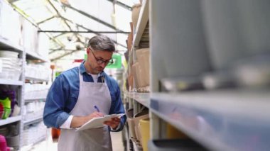 Ciddi gri saçlı çiçekçi evin içindeki saksıları kontrol edip yazıyor.