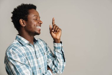 Ekose gömlekli siyahi adam gülerken, beyaz arka planda yalnız bir şekilde parmağını yukarı kaldırıyor.