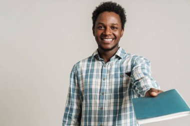 Ekose gömlekli, siyah traşsız bir adam beyaz arka planda izole bir egzersiz kitabıyla poz veriyor.