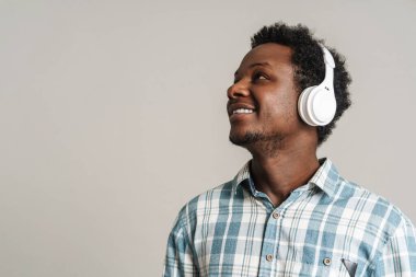 Beyaz arka planda izole edilmiş kulaklıklarla müzik dinlerken gülümseyen siyah adam.