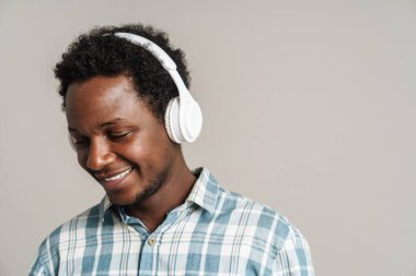 Beyaz arka planda izole edilmiş kulaklıkla müzik dinlerken gülümseyen genç bir zenci.