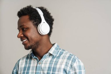 Beyaz arka planda izole edilmiş kulaklıklarla müzik dinlerken gülümseyen siyah adam.