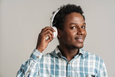 Beyaz arka planda izole edilmiş kulaklıklarla müzik dinlerken gülümseyen siyah adam.