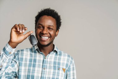 Beyaz arka planda izole edilmiş araba anahtarlarıyla poz veren siyah traşsız adam gülüyor.