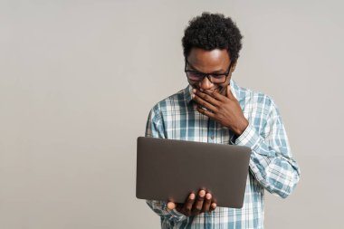 Gözlüklü siyah adam beyaz arka planda dizüstü bilgisayarla çalışırken gülümsüyor.