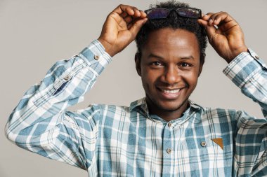 Siyah gözlüklü genç adam gülümsüyor ve beyaz arka planda izole edilmiş kameraya bakıyor.