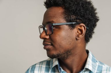 Siyah gözlüklü genç adam beyaz arka planda yalnız poz veriyor ve yan bakıyor.