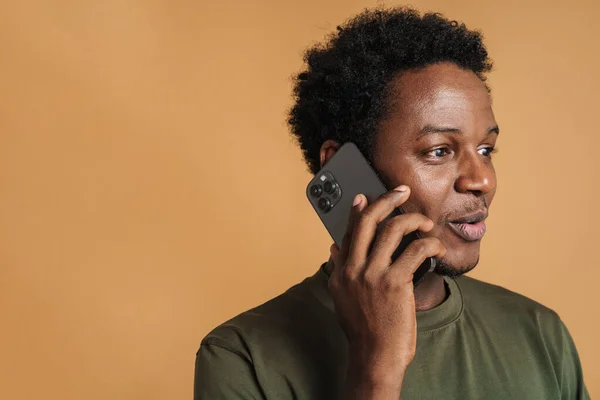 Молодой Чернокожий Мужчина Выражает Удивление Разговаривая Мобильному Телефону Изолированы Бежевом — стоковое фото