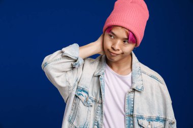 Pembe şapkalı Asyalı çocuk mavi arka planda soyutlanmış ve yan bakıyor.