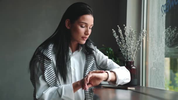Pozytywne Młoda Brunetka Kobieta Patrząc Smartwatch Okno Podczas Siedzenia Kawiarni — Wideo stockowe