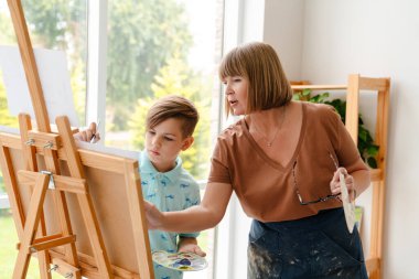 Sanat okulunda sınıf boyunca öğrencileriyle konuşan beyaz bir öğretmen.