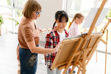 Sanat okulunda sınıf boyunca öğrencileriyle konuşan beyaz bir öğretmen.