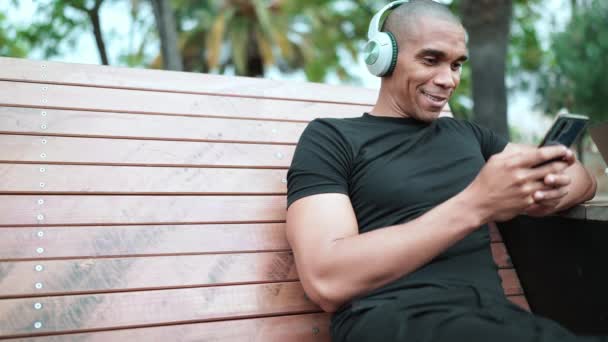 Glada Skallig Afrikansk Man Skriva Telefon Hörlurar Medan Sitter Bänken — Stockvideo