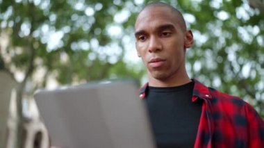 Dışarıdaki bankta dijital tablette yazan dalgın, kel bir Afrikalı.