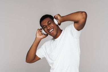 Gri duvarda izole edilmiş kulaklıklarla müzik dinleyen genç bir zenci.