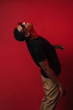 Güneş gözlüğü takan genç bir adam çığlık atıyor ve kırmızı duvarın üzerinden yukarı bakıyor.