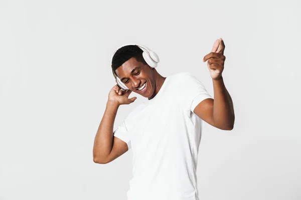 白い壁の上に隔離されたヘッドフォンで音楽を聞きながら若い黒人男性が踊る — ストック写真