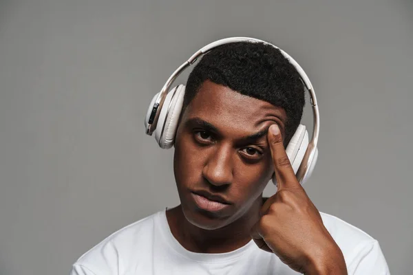 Young black man in headphones pointing finger at his temple isolated over grey wall