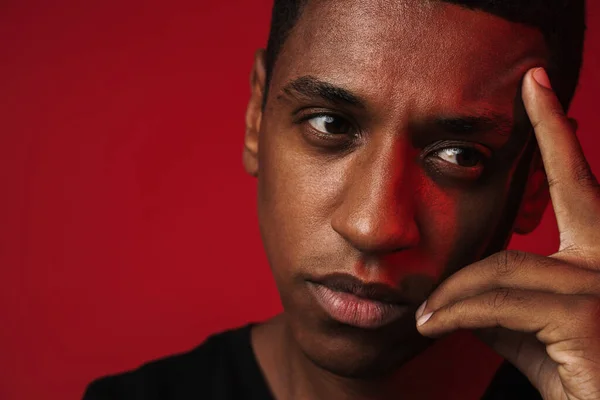 Young black man pointing finger at his temple and looking aside isolated over red wall