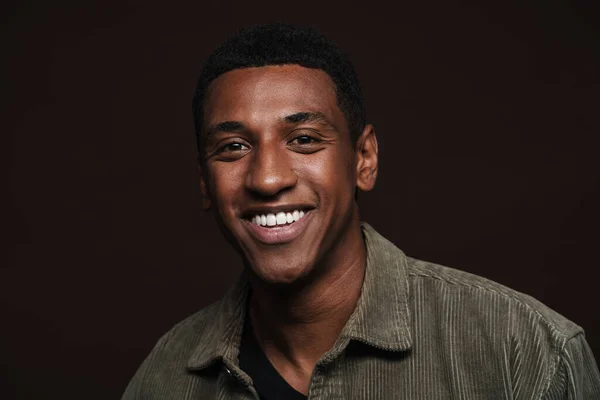 Young black man dressed in shirt smiling and looking aside isolated over brown wall