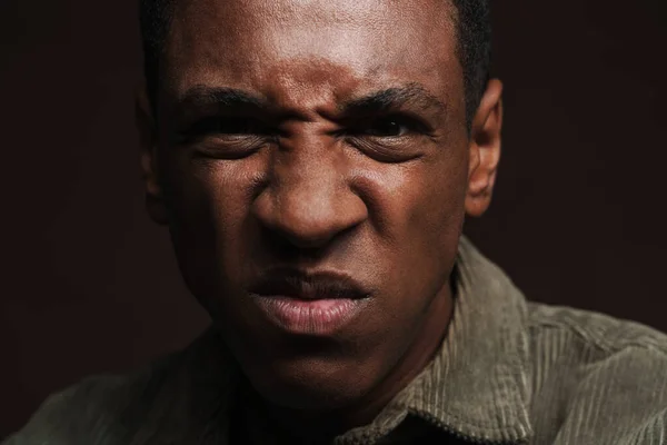 Young black man frowning and looking at camera isolated over brown wall