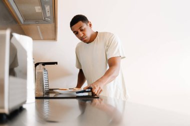 Otelde kahvaltı hazırlarken cep telefonu kullanan tişörtlü siyah bir adam.