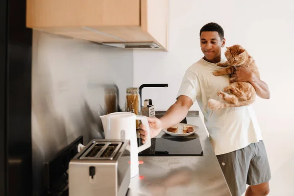 Black man wearing t-shirt holding his cat while making breakfast in hotel