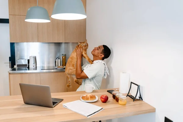 Black man playing with his cat while having breakfast in hotel