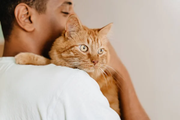 Black man wearing t-shirt smiling while petting his cat in hotel