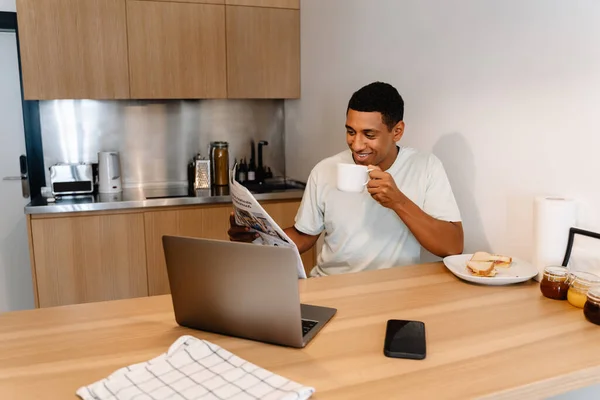 Black Man Reading Newspaper Drinking Coffee While Working Laptop Hotel — Stock Photo, Image