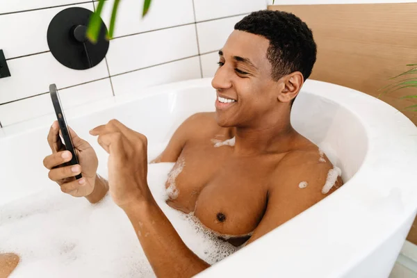 Μαύρος Άντρας Χαμογελά Και Χρησιμοποιεί Κινητό Ενώ Κάνει Μπάνιο Αφρό — Φωτογραφία Αρχείου