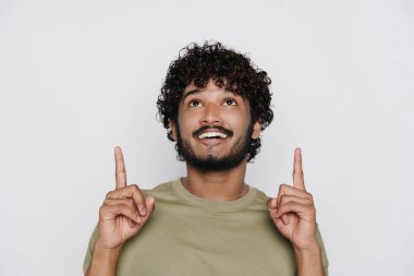 Genç sakallı adam gülümsüyor ve beyaz arka planda parmaklarını yukarı kaldırıyor.