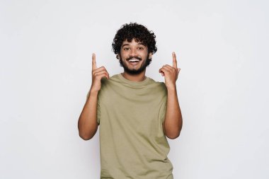 Orta Doğulu genç adam gülümsüyor ve parmaklarını yukarı doğru gösteriyor. Beyaz duvarın üzerinden soyutlanmış.