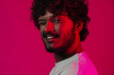 Young middle eastern man smiling and winking at camera isolated over pink wall