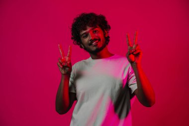 Young middle eastern man smiling and showing peace sign isolated over pink wall